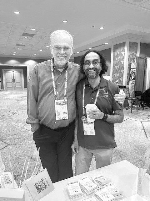 Tashu posing with a colleague at a conference. Both wear nametags and are smiling.