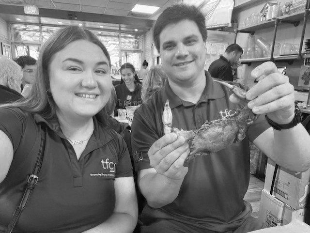 Photo of Kira and Nick sitting together at a restaurant; Nick is holding a crab up to the camera and smiling.